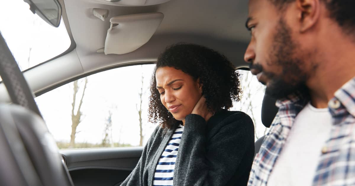 a woman in pain holds her neck after a car crash | Burg Simpson