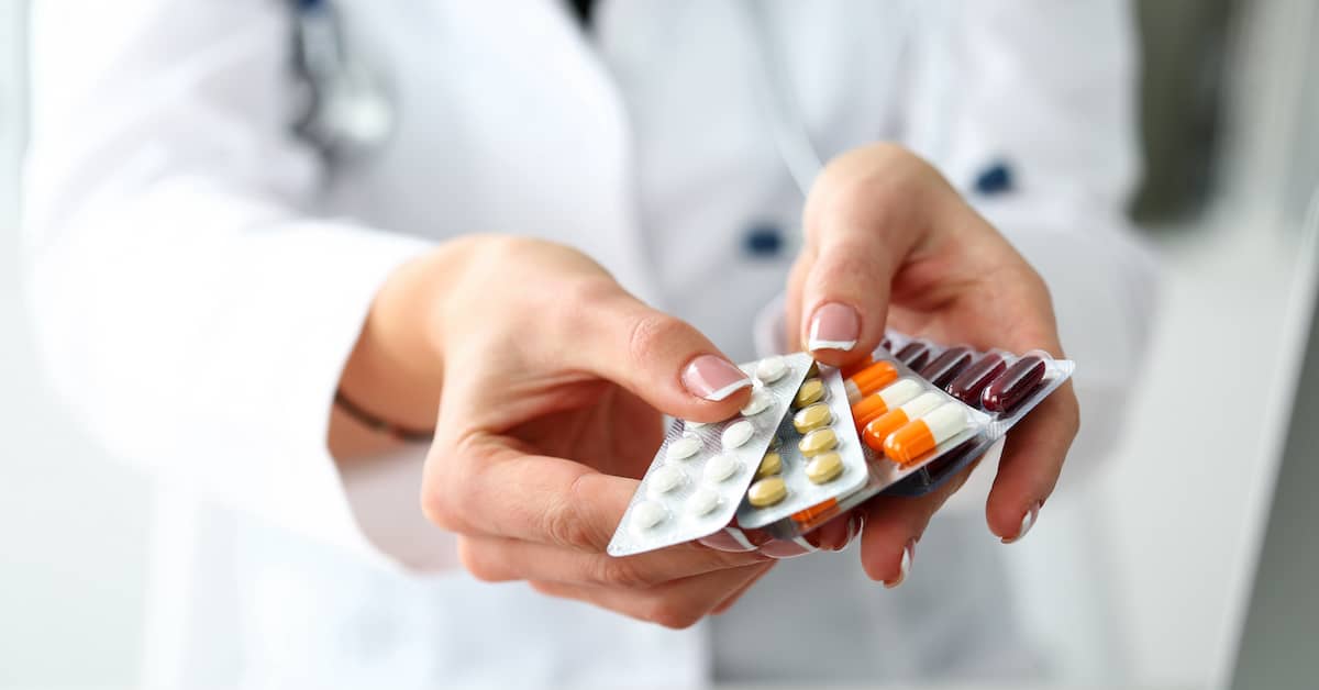 Doctor holding blister packs of different medications | Burg Simpson