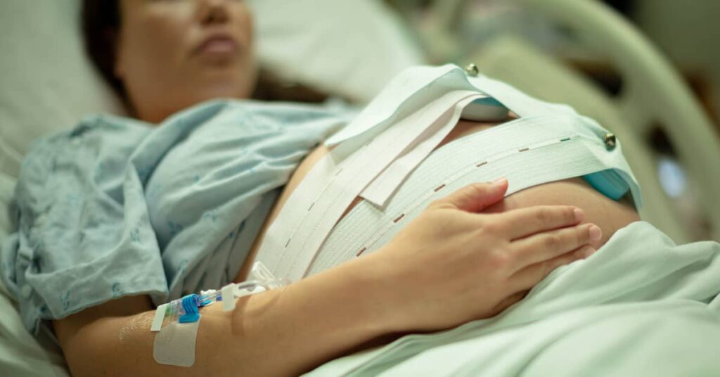 a pregnant woman holds her belly in a hospital bed | Burg Simpson