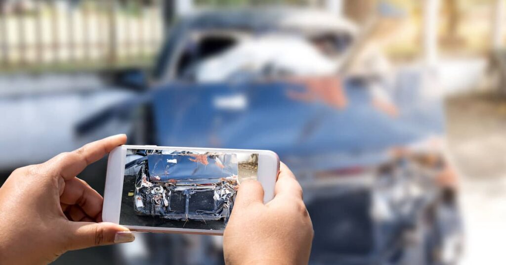 Woman taking a picture of her car after an accident using a mobile phone | Burg Simpson