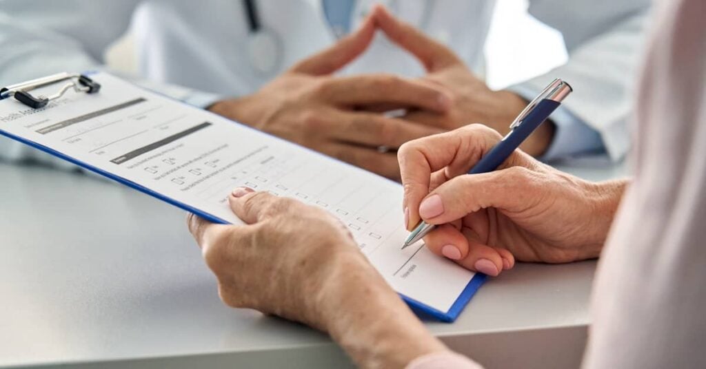 Senior woman filling out health insurance paperwork at doctor's office | Burg Simpson Law Firm