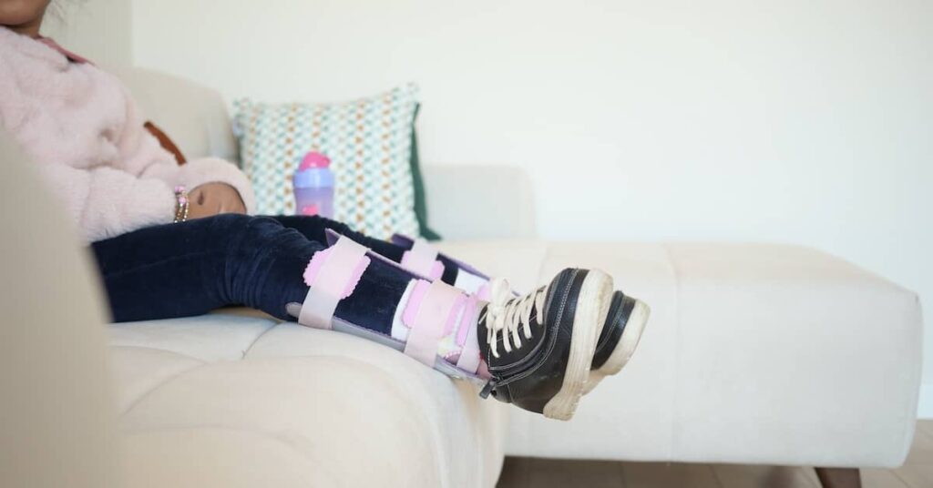 Little girl with cerebral palsy sitting on sofa wearing leg orthotics | Burg Simpson