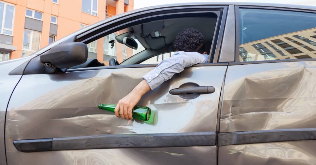 Drunk driver leaning out the window of the car after an accident | Burg Simpson