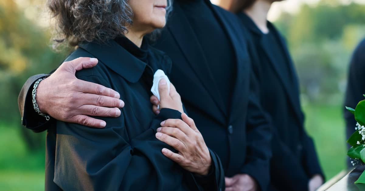 One mourner comforting another at a funeral for a loved one | Burg Simpson