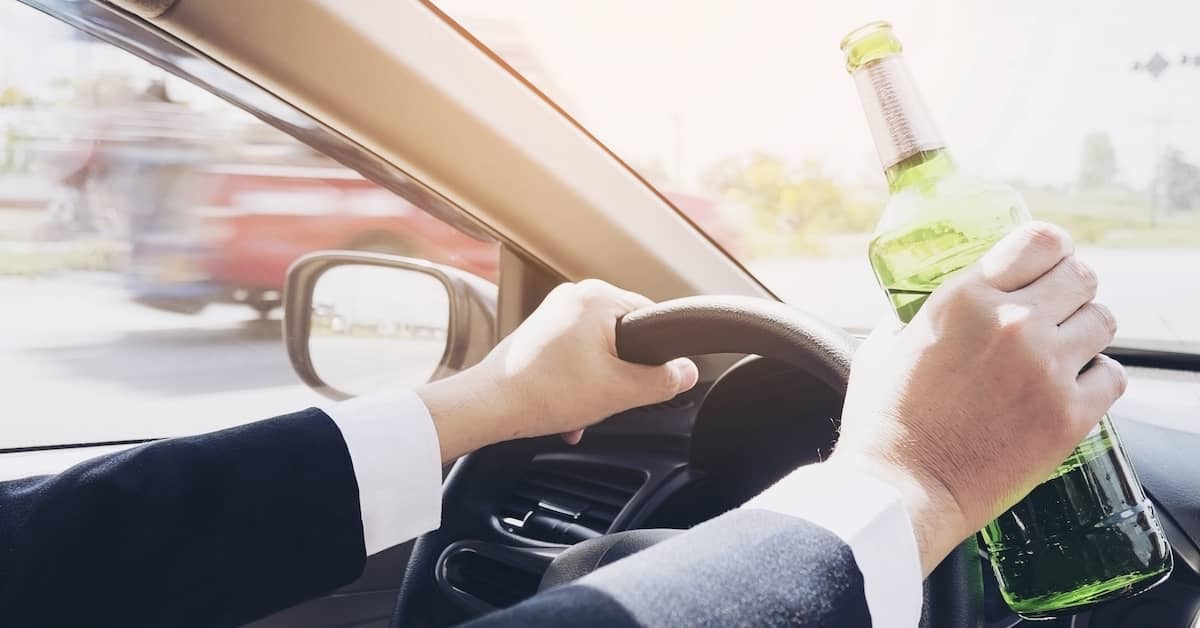 Drunk driver behind the wheel of a car with a liquor bottle in his hand | Burg Simpson