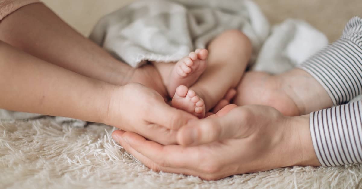 New father and mother holding newborn baby's feet | Burg Simpson