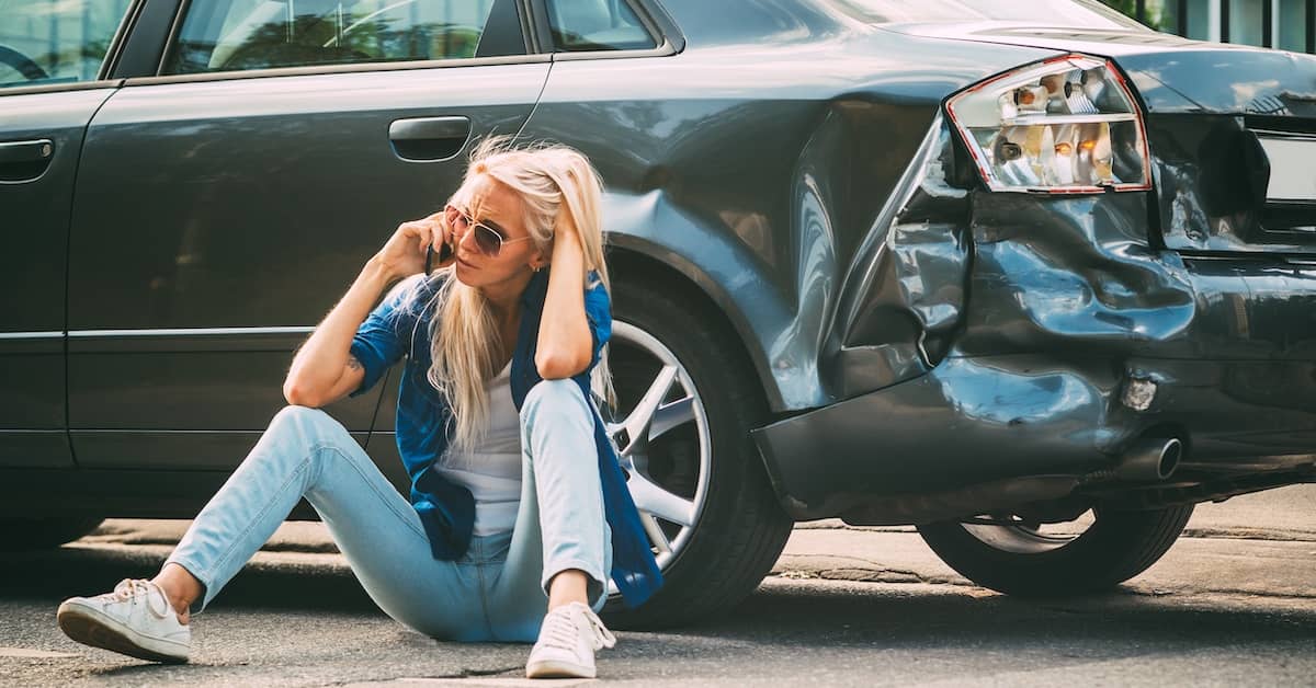 Woman sitting by her car distressed after a car accident | Burg Simpson